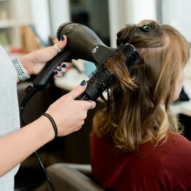 Hairdresser blow drying and brushing hair